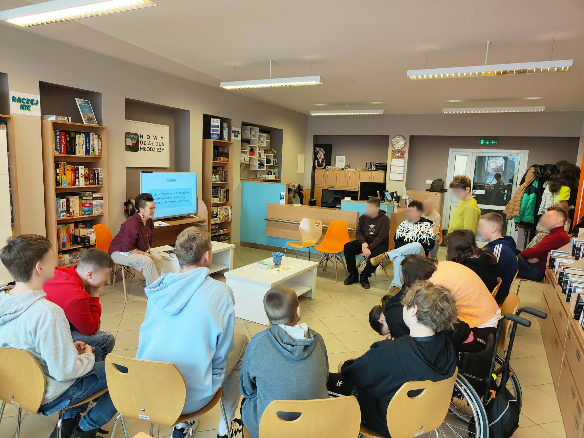 Zajęcia edukacyjne w dziale NASTKA – młodzież siedzi w kręgu, prowadząca omawia temat przy ekranie.