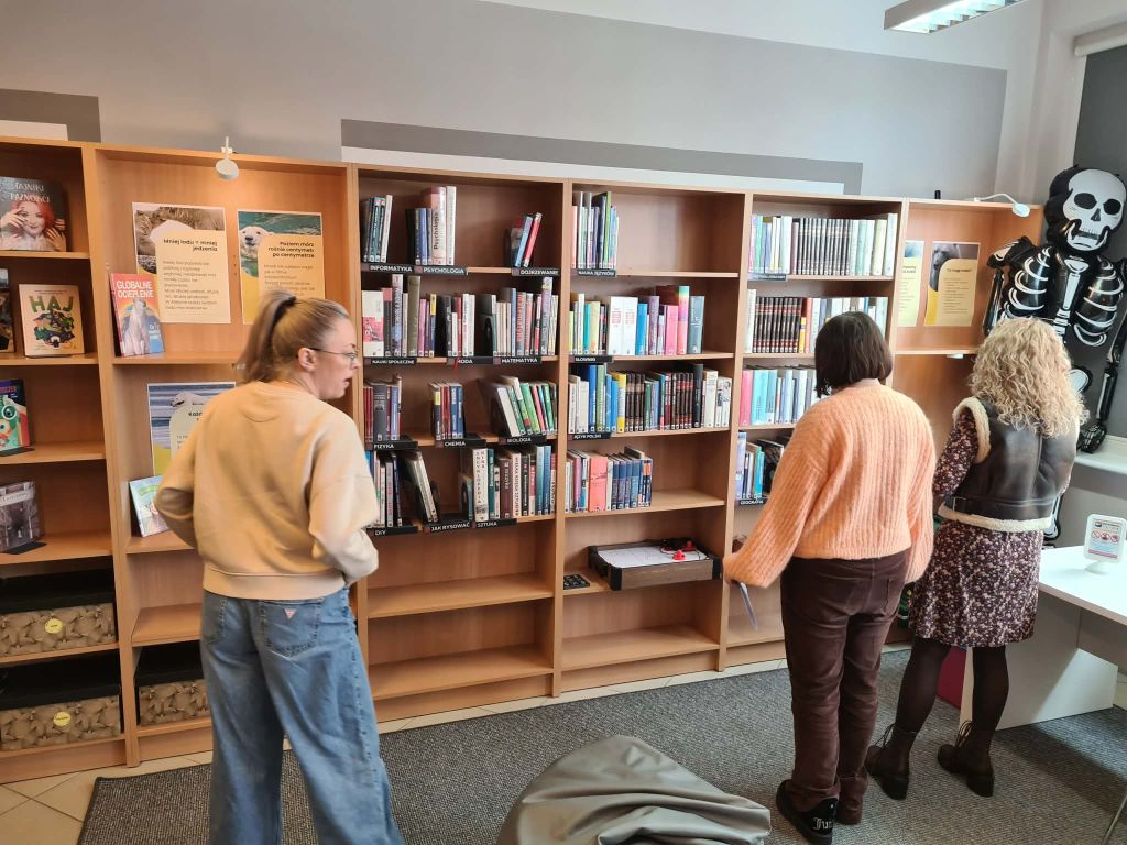 Czytelnicy przy regale z książkami popularnonaukowymi i planszami klimatycznymi.