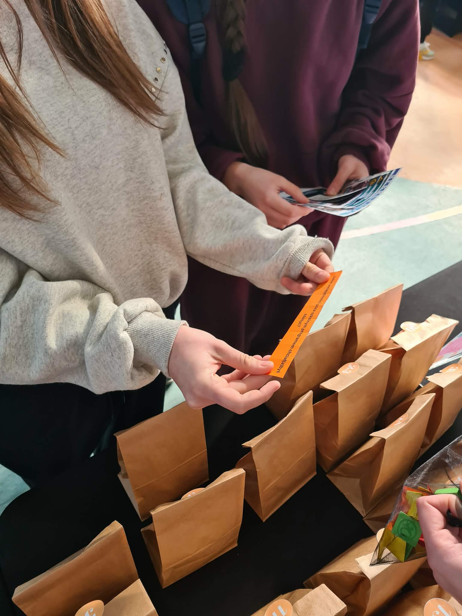 Uczestnicy wydarzenia losują nagrody z papierowych torebek przy stoisku biblioteki.