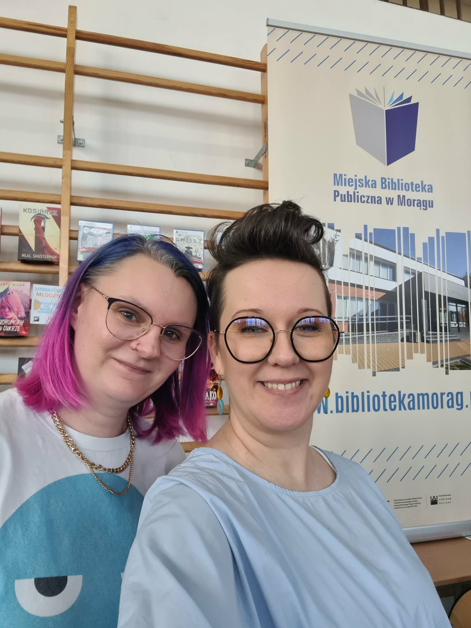 Pracowniczki biblioteki robią selfie przy stoisku promocyjnym Miejskiej Biblioteki Publicznej w Morągu.