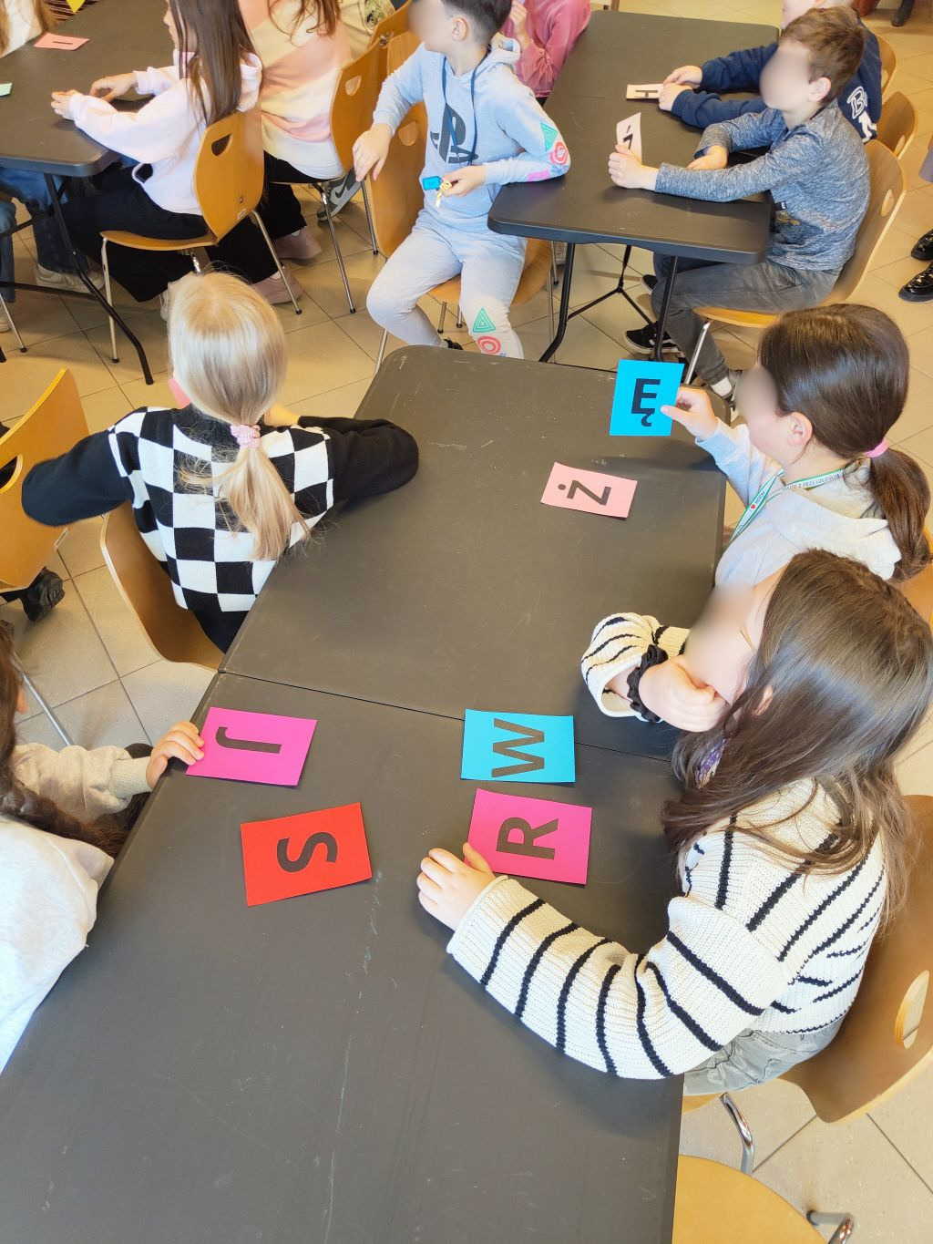 Widok z góry na dzieci siedzące przy czarnym stole i układające słowa z kolorowych kart z literami.
