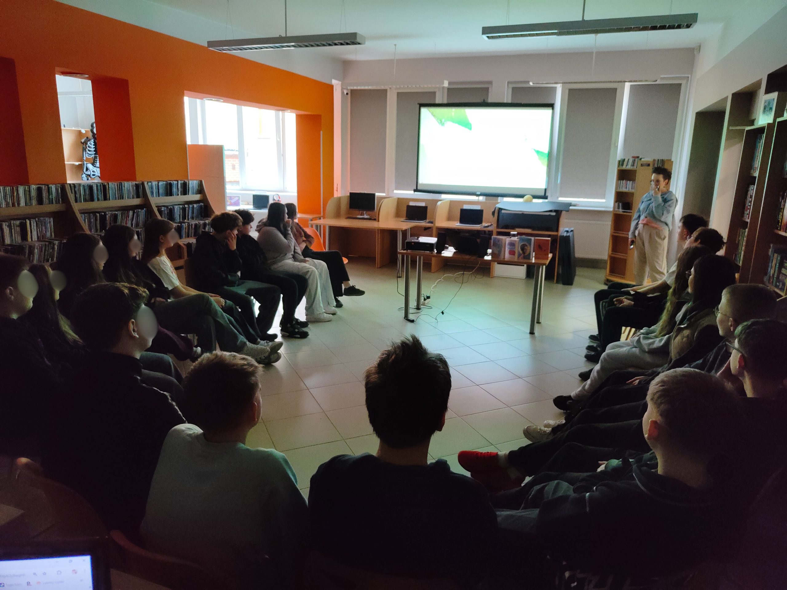 Młodzież siedząca w kręgu na krzesłach w jasnej sali bibliotecznej.