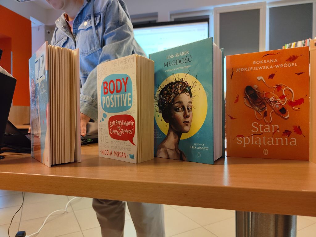Cztery książki o tematyce młodzieżowej i ciałopozytywności ustawione na drewnianym stole.