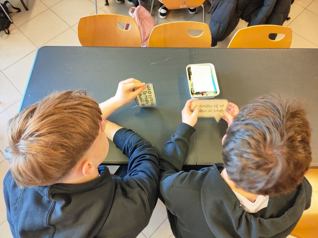 Dwóch chłopców przy czarnym stoliku analizuje papierowe dymki z zadaniami do posegregowania według priorytetów.