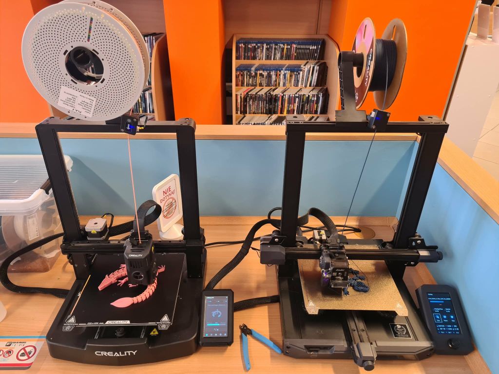 Dwie drukarki 3D pracujące obok siebie podczas zajęć w bibliotece.