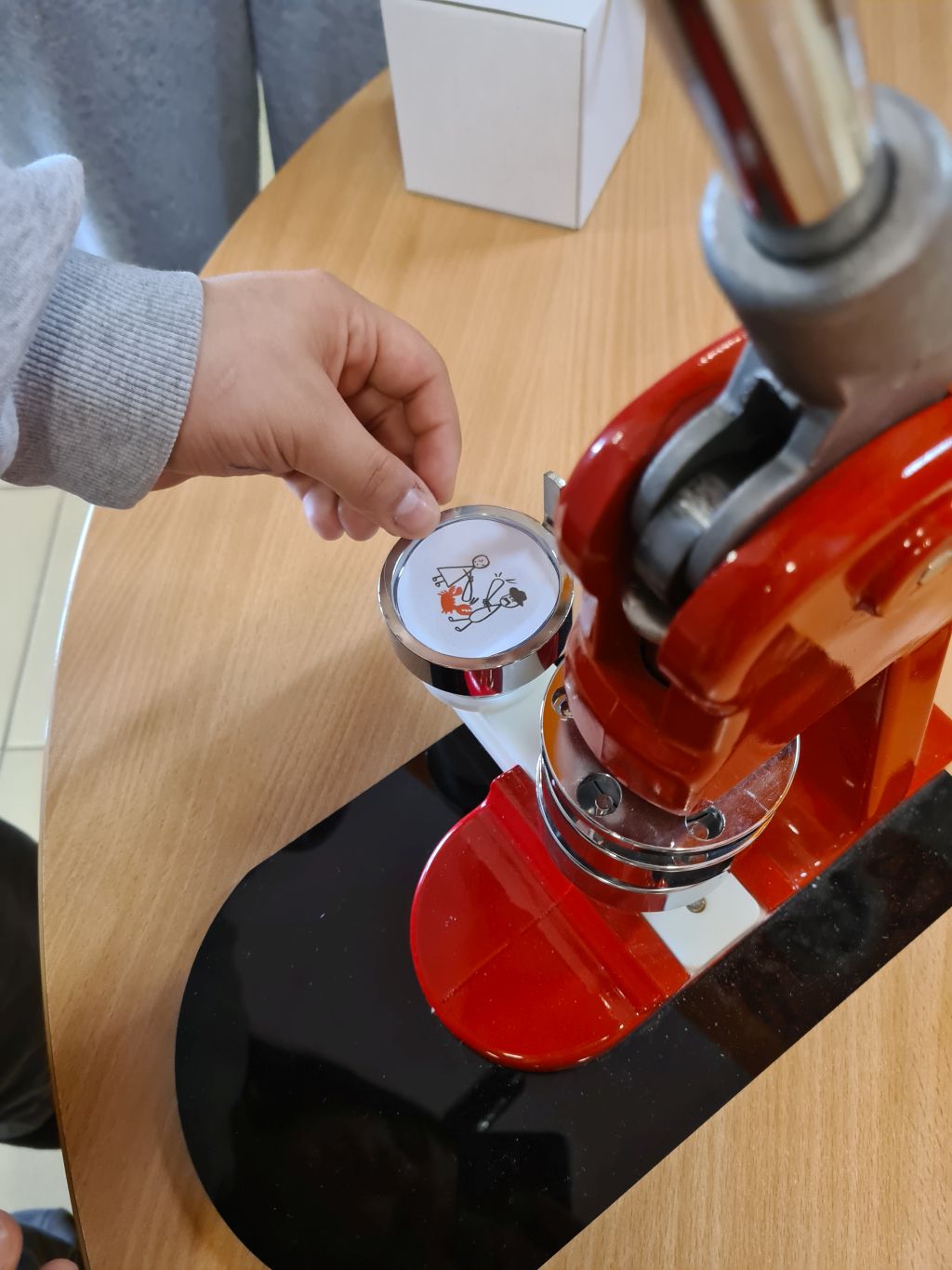 Dziecko umieszcza wyciętą grafikę w metalowej formie czerwonej prasy do robienia przypinek.