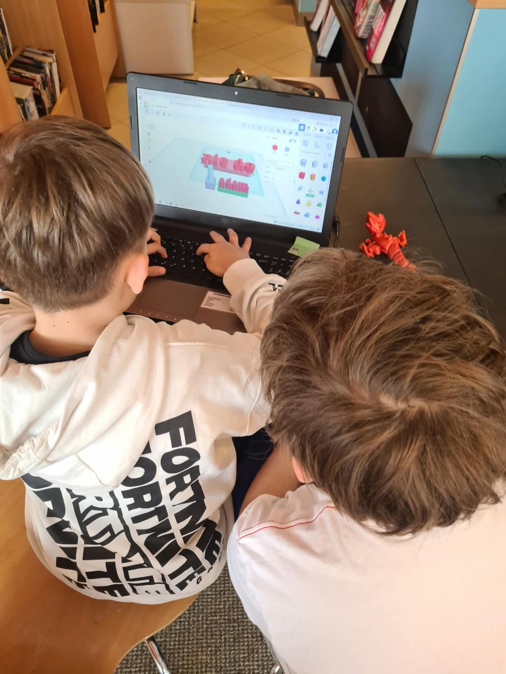 Dwoje dzieci projektuje model 3D na laptopie podczas warsztatów.