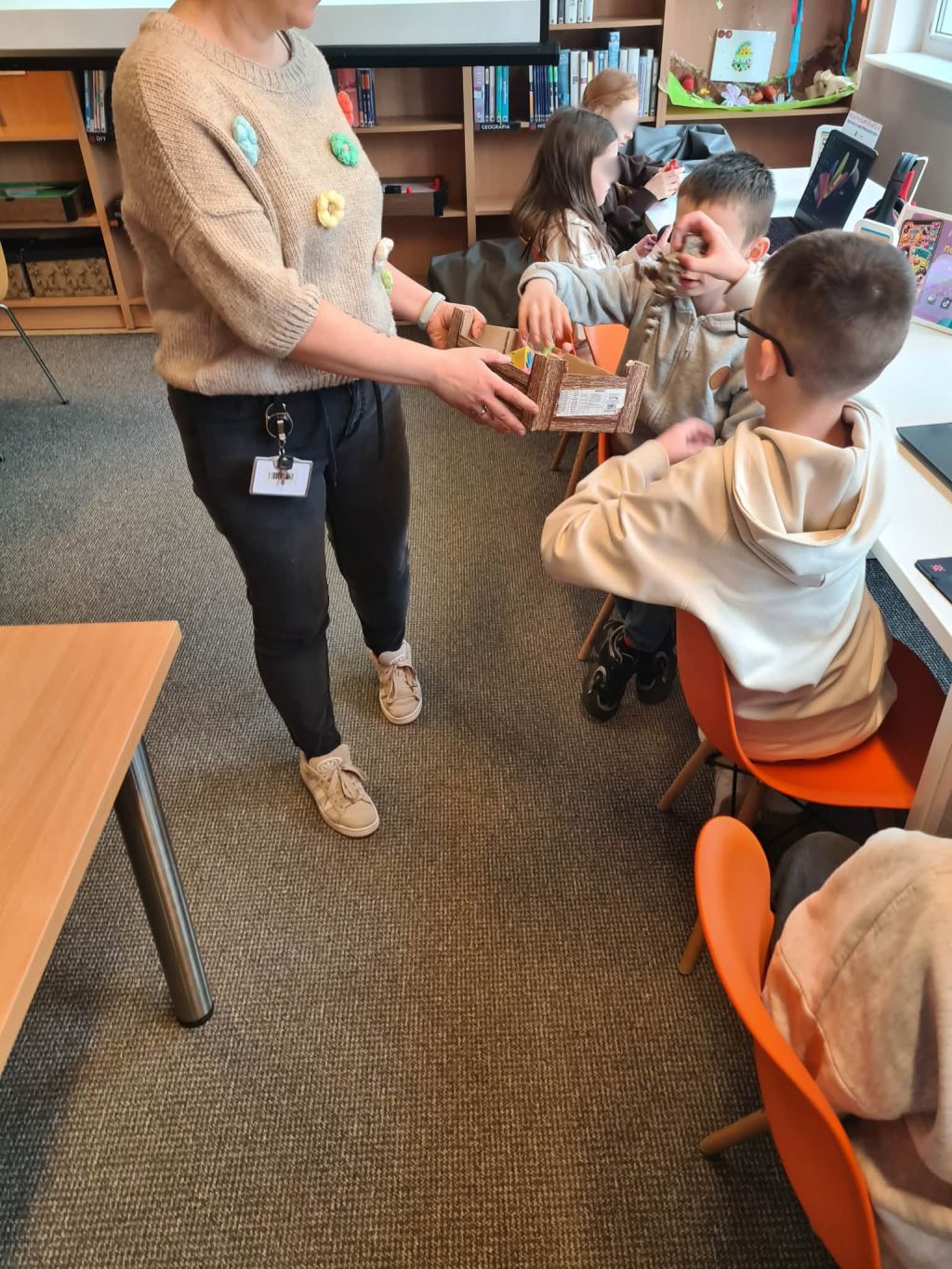 Prowadząca rozdaje dzieciom wydruki 3D podczas zajęć w bibliotece.