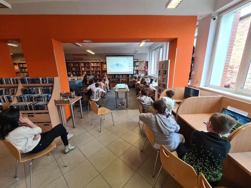 Uczestnicy warsztatów siedzą w sali bibliotecznej i oglądają prezentację o projektowaniu 3D.