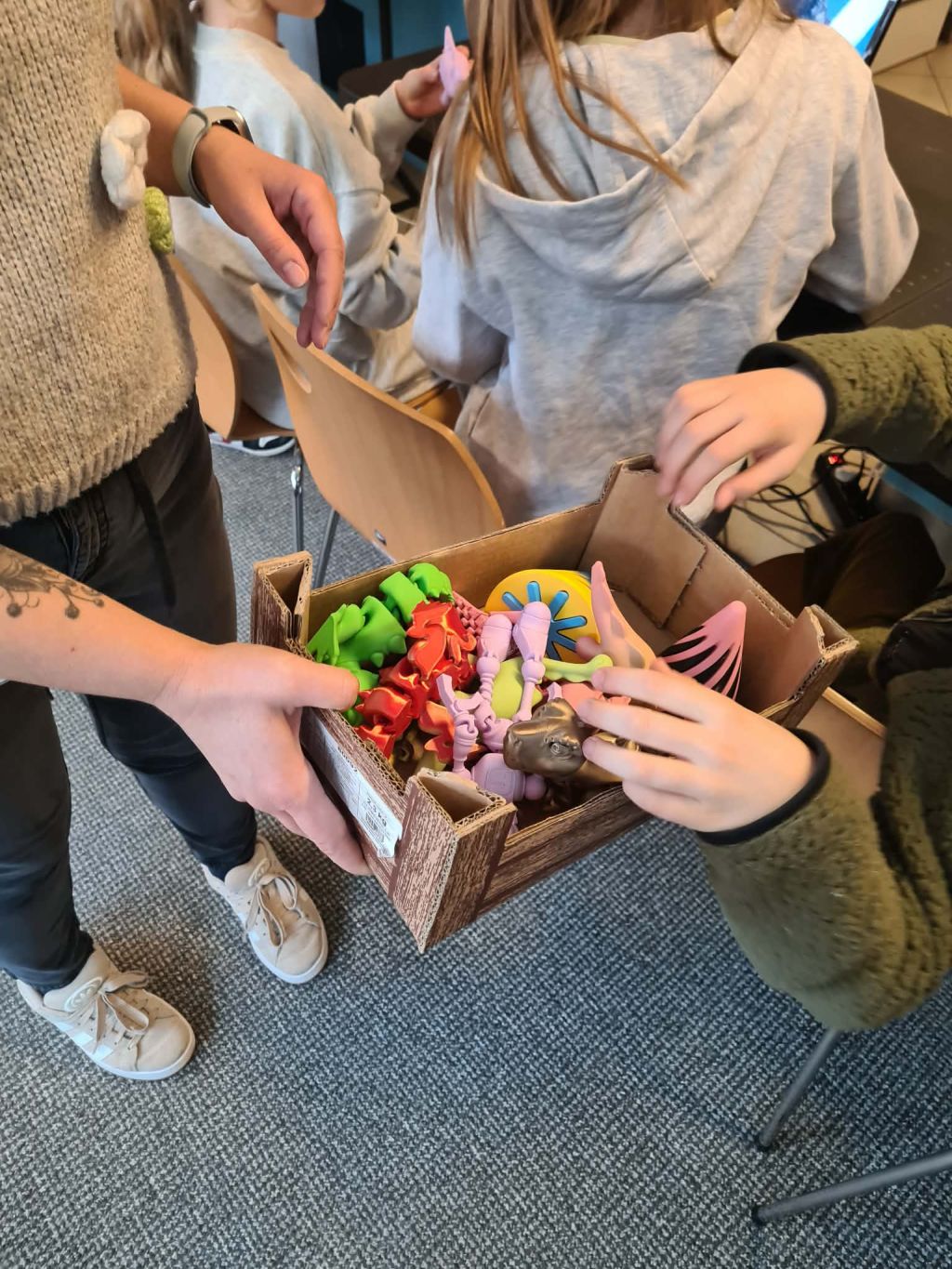 Dzieci oglądają kolorowe wydruki 3D w pudełku trzymanym przez prowadzącą.