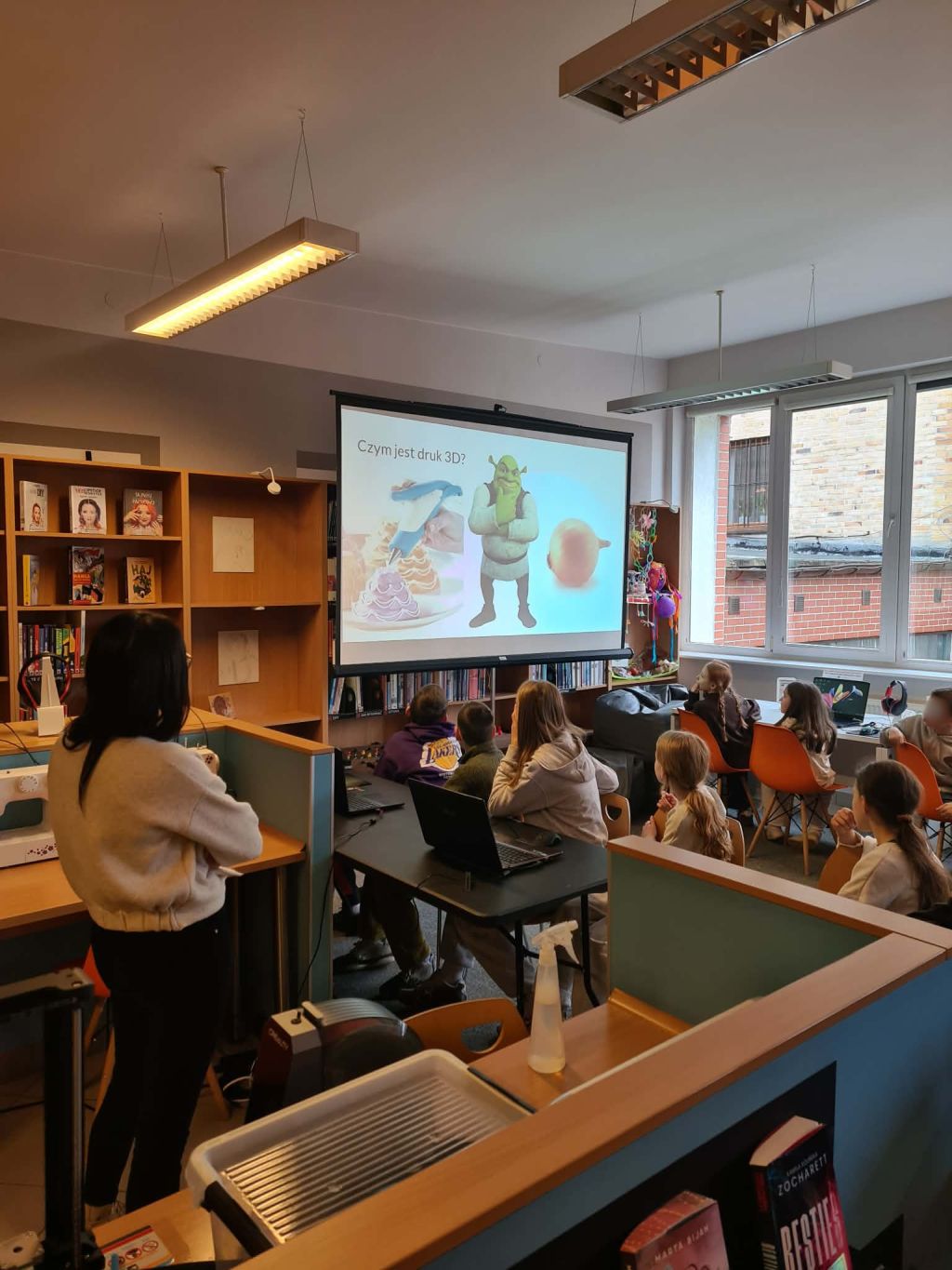 Prezentacja o druku 3D wyświetlana na ekranie podczas warsztatów dla dzieci w bibliotece.