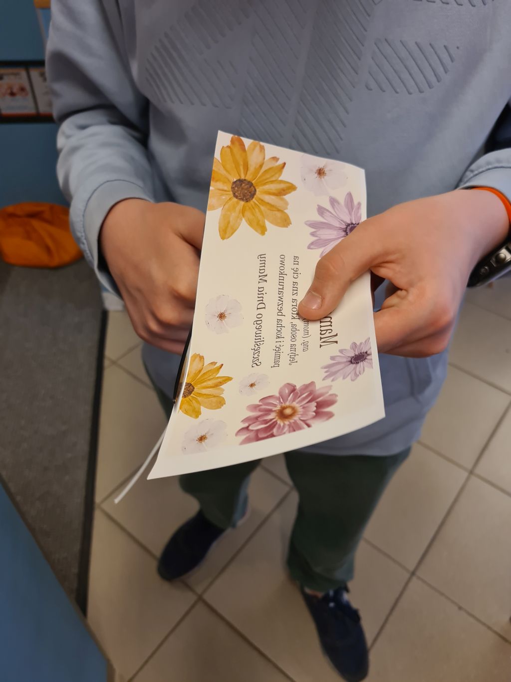 Bliskie ujęcie na dłonie osoby trzymającej wydrukowany szablon z motywami kwiatowymi i napisami dedykowanymi mamie.