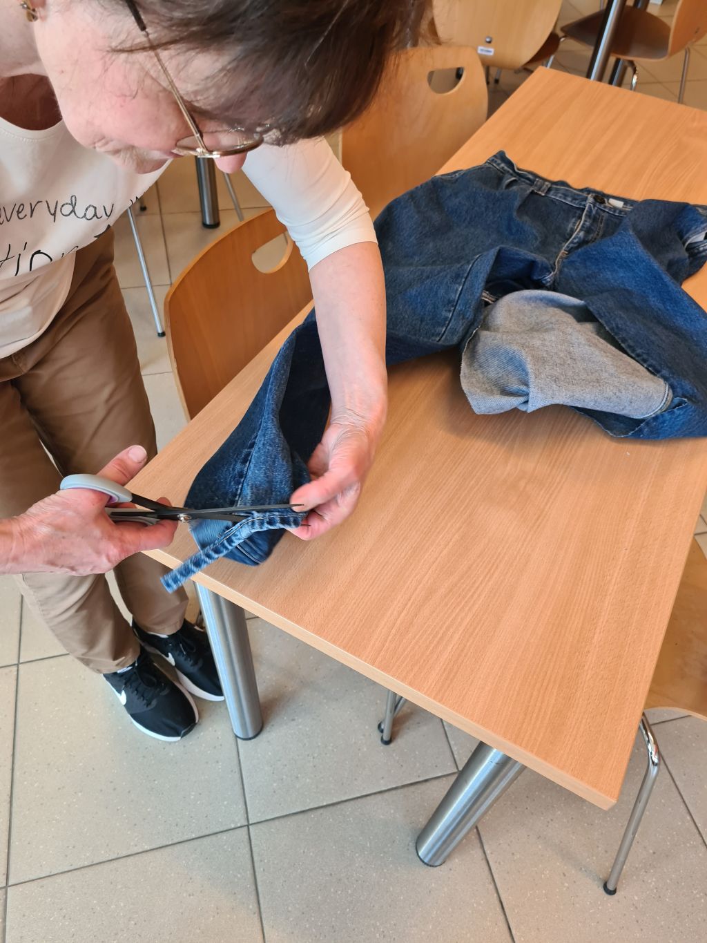 Uczestniczka warsztatów odcina fragment nogawki jeansów, przygotowując materiał do uszycia torby.