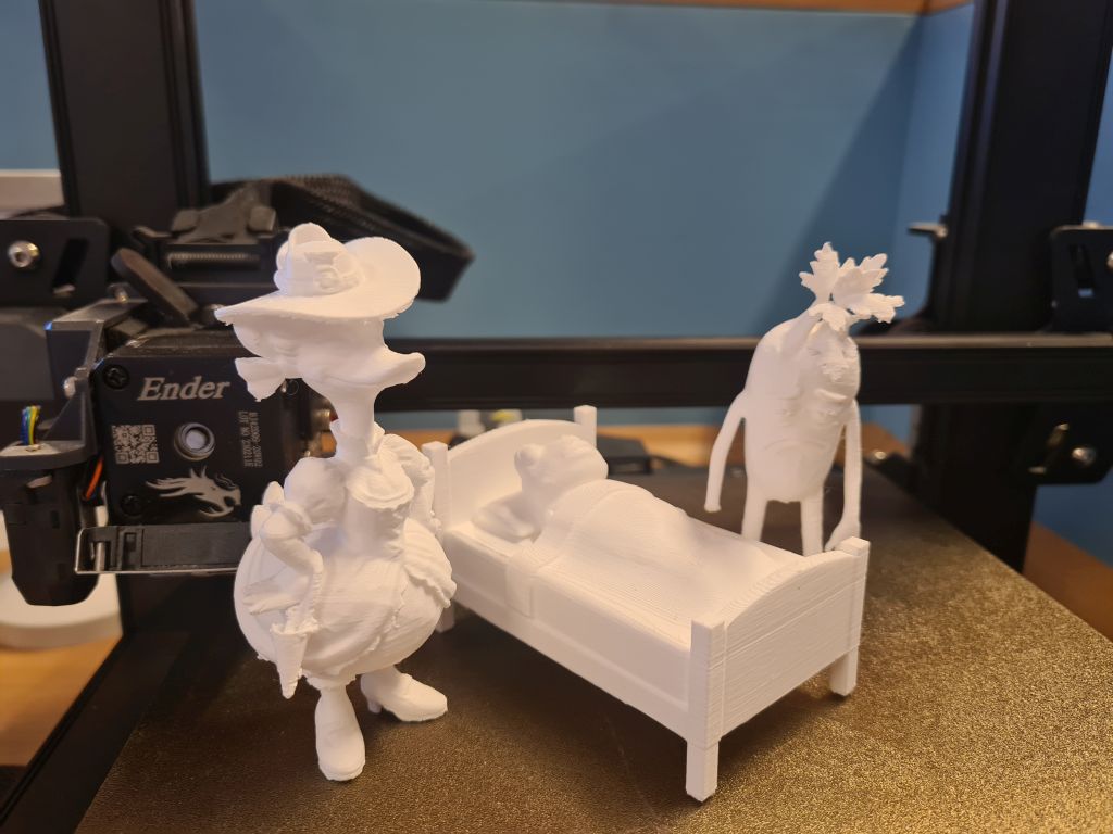 Białe wydruki 3D postaci inspirowanych literaturą stoją na stole roboczym drukarki 3D.