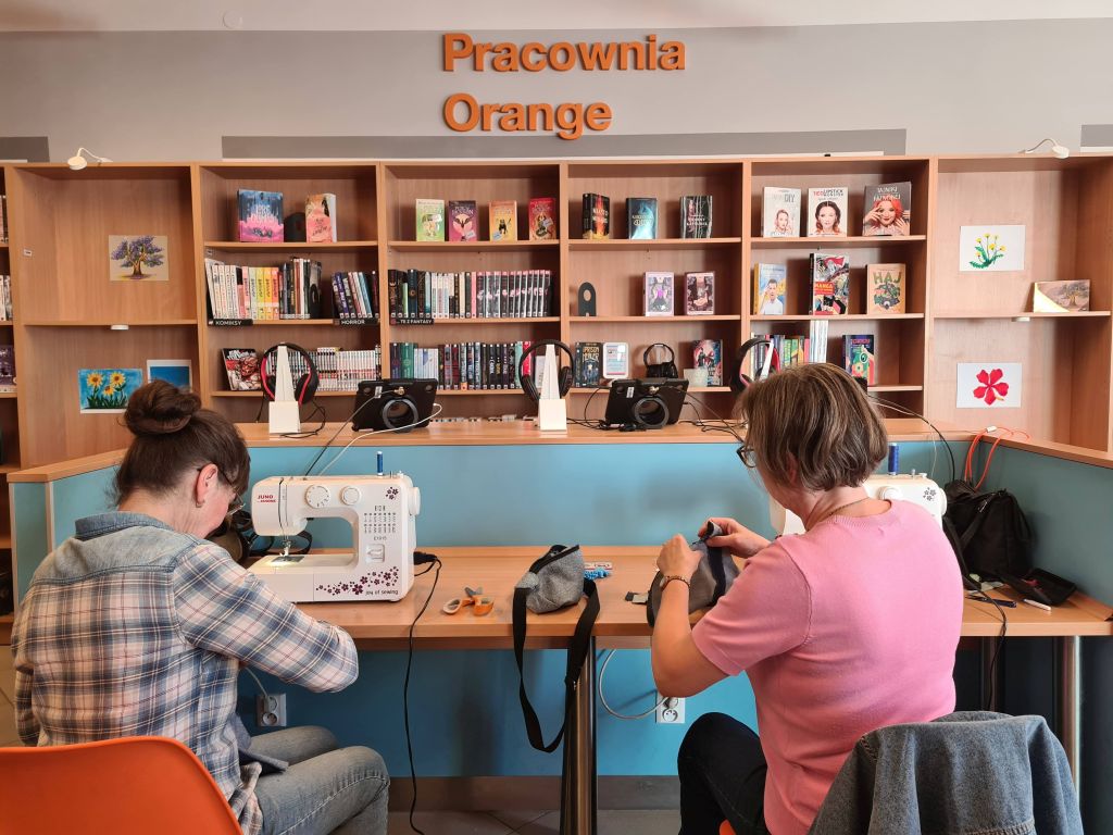 Uczestniczki warsztatów pracują przy maszynach do szycia w Pracowni Orange, przygotowując własne nerki z odzyskanych materiałów.