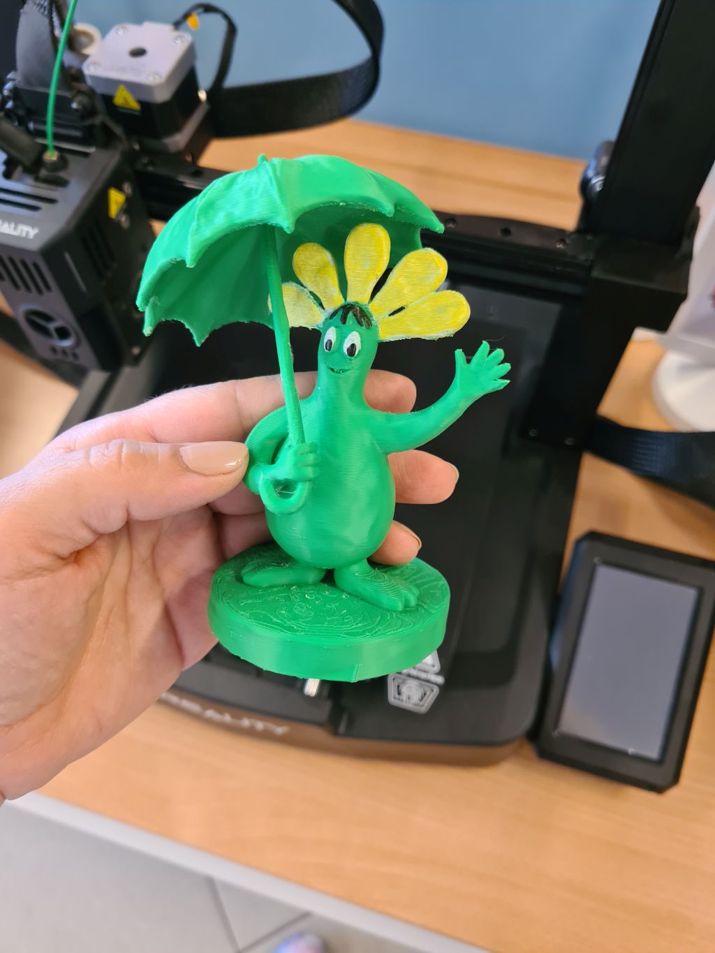 Kolorowa figurka wydrukowana na drukarce 3D trzymana na tle drukarki.