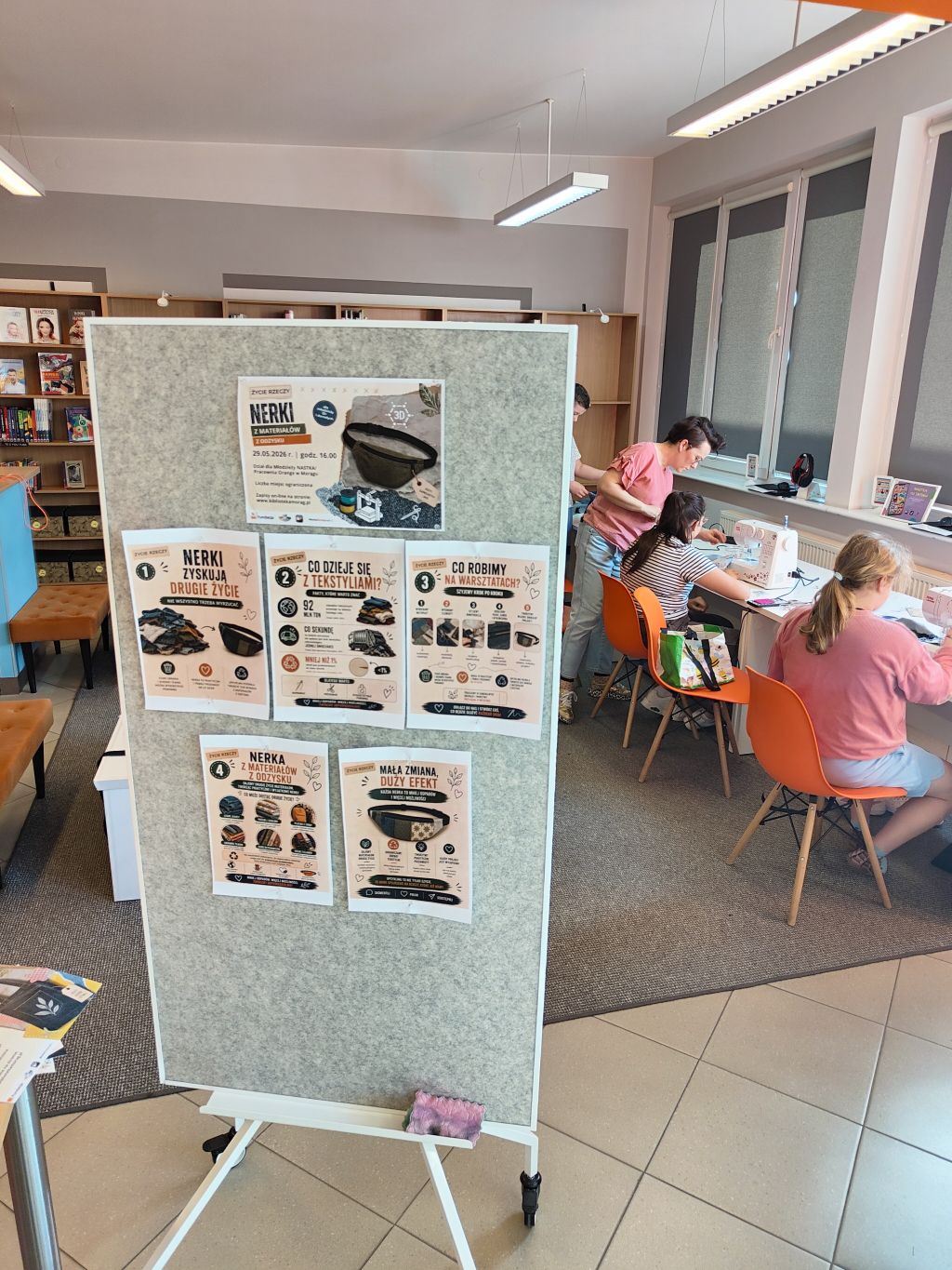 ablica informacyjna o warsztatach „Nerki z materiałów z odzysku” w ramach projektu „Życie rzeczy”. W tle uczestnicy szyją przy stanowiskach.