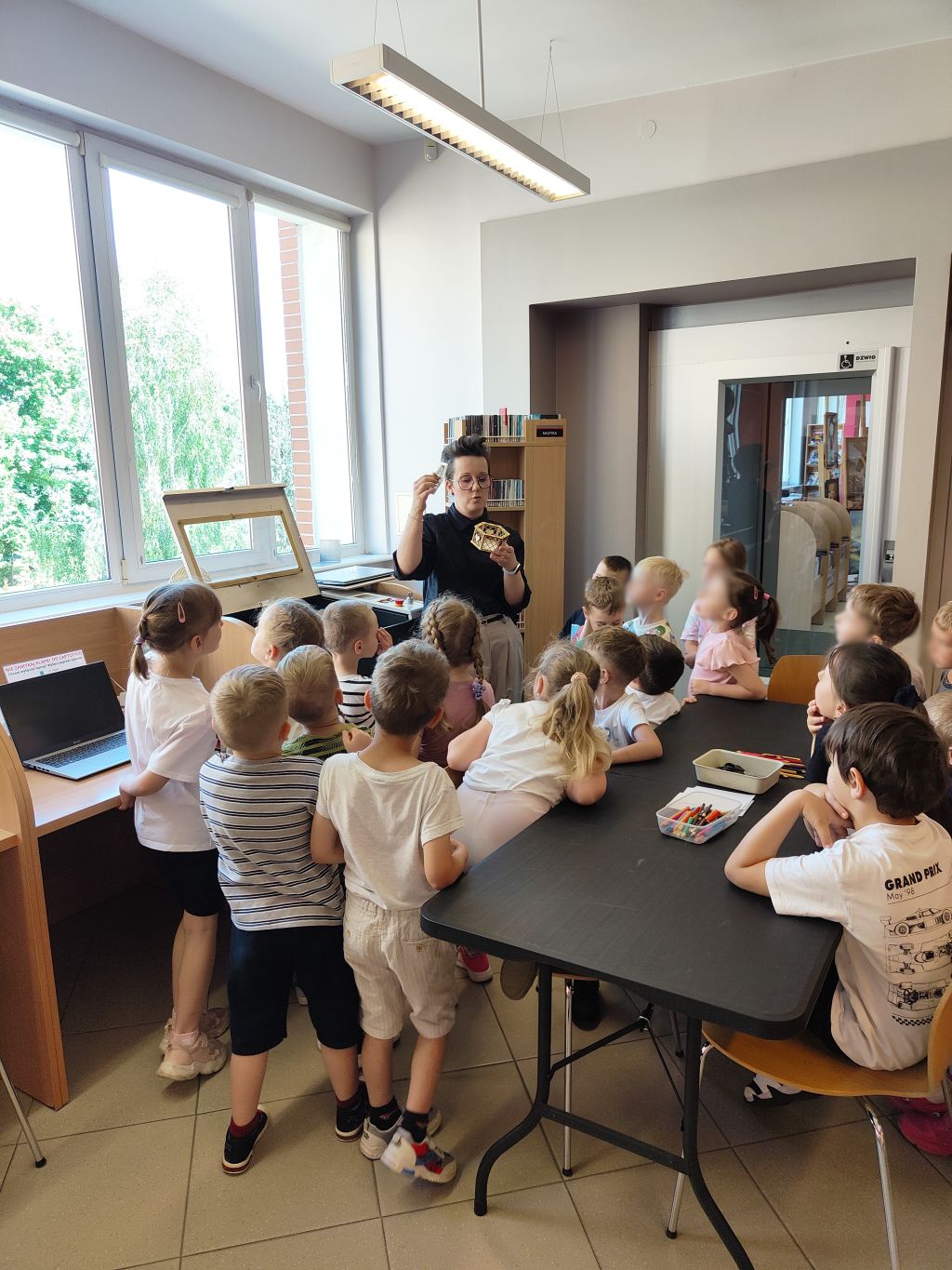 Dzieci słuchają opowieści o ploterze laserowym i drewnianych elementach.