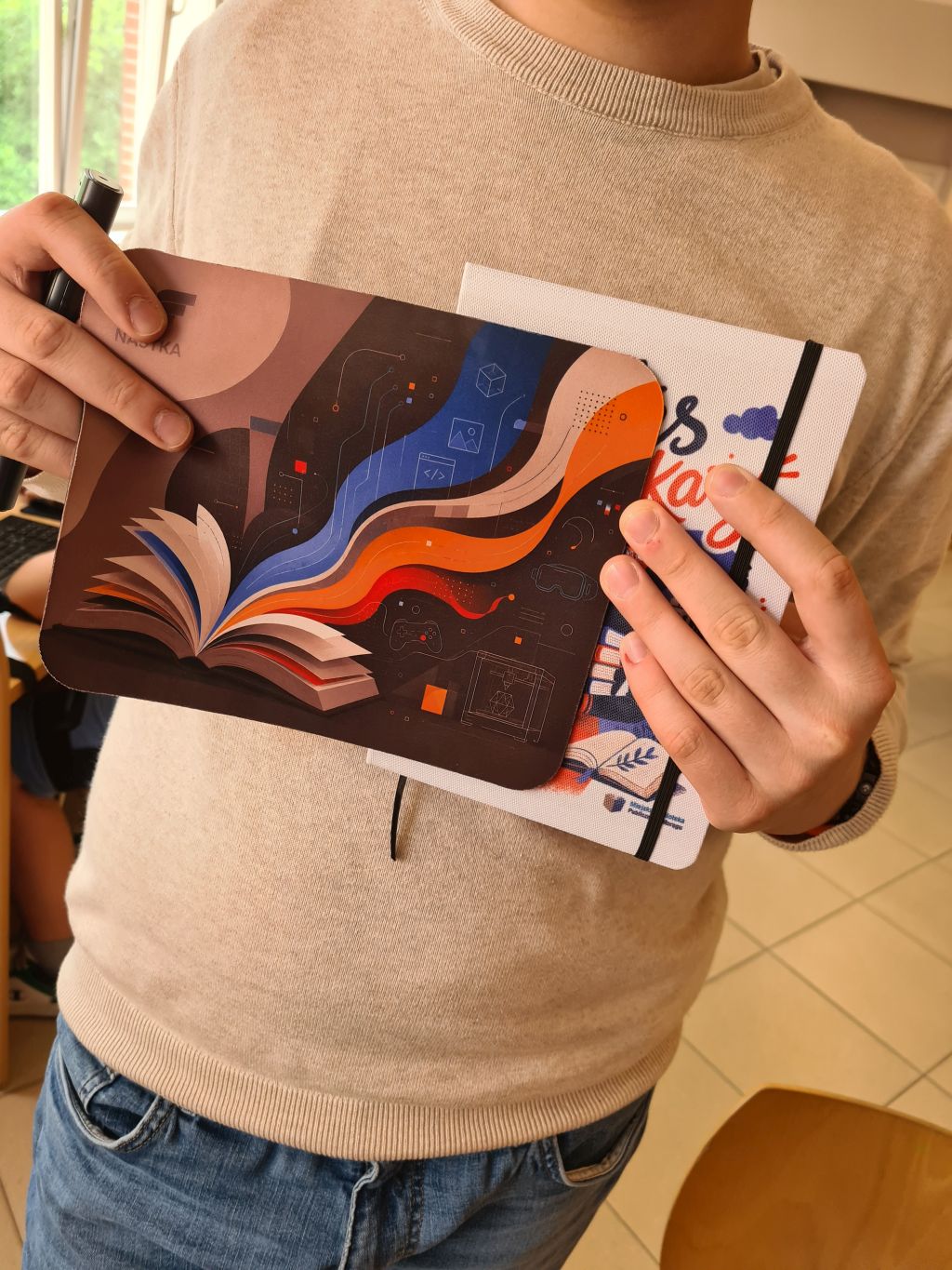 Uczestnik trzyma autorski notes i podkładkę pod myszkę.