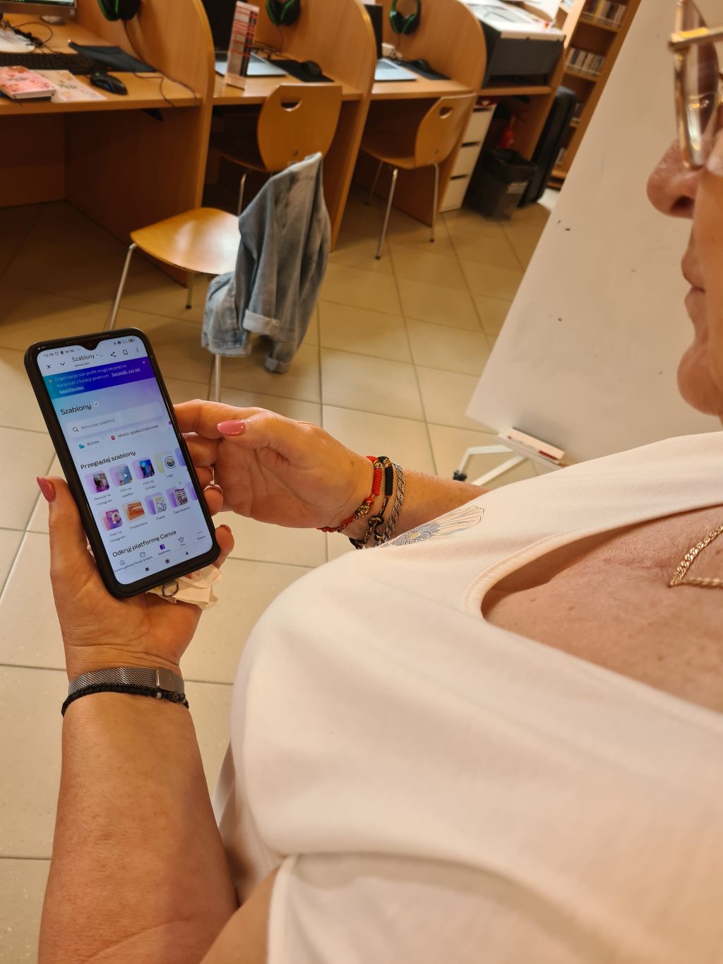 Uczestniczka warsztatów korzysta ze smartfona z otwartą aplikacją Canva i przegląda dostępne szablony graficzne.