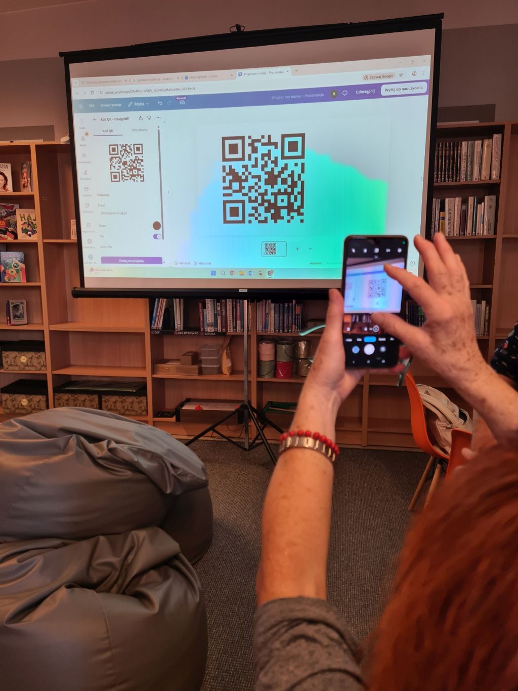 Uczestniczka skanuje telefonem kod QR wyświetlony na ekranie podczas zajęć TechnoSenior.