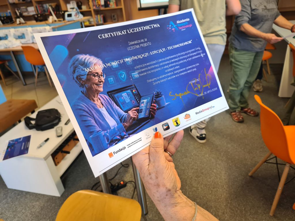 Uczestniczka trzyma certyfikat ukończenia cyklu TechnoSenior realizowanego w ramach Akademii Nowych Technologii.
