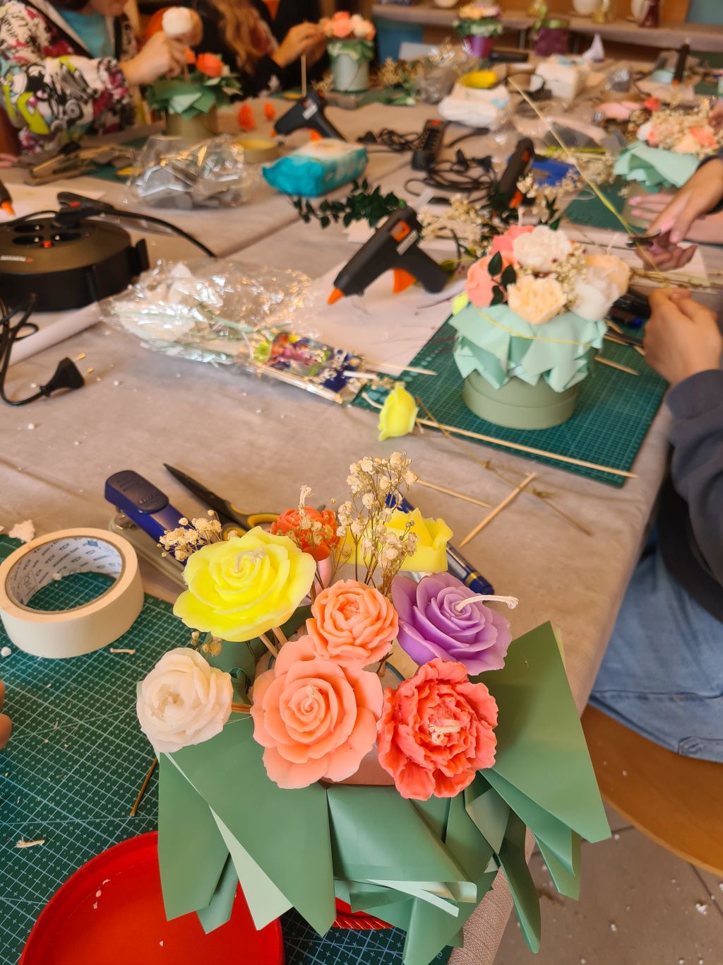 Kilka flowerboxów w trakcie wykonywania. Na pierwszym planie kompozycja z żółtych, koralowych i fioletowych świec-kwiatów oraz zielonych papierowych liści.