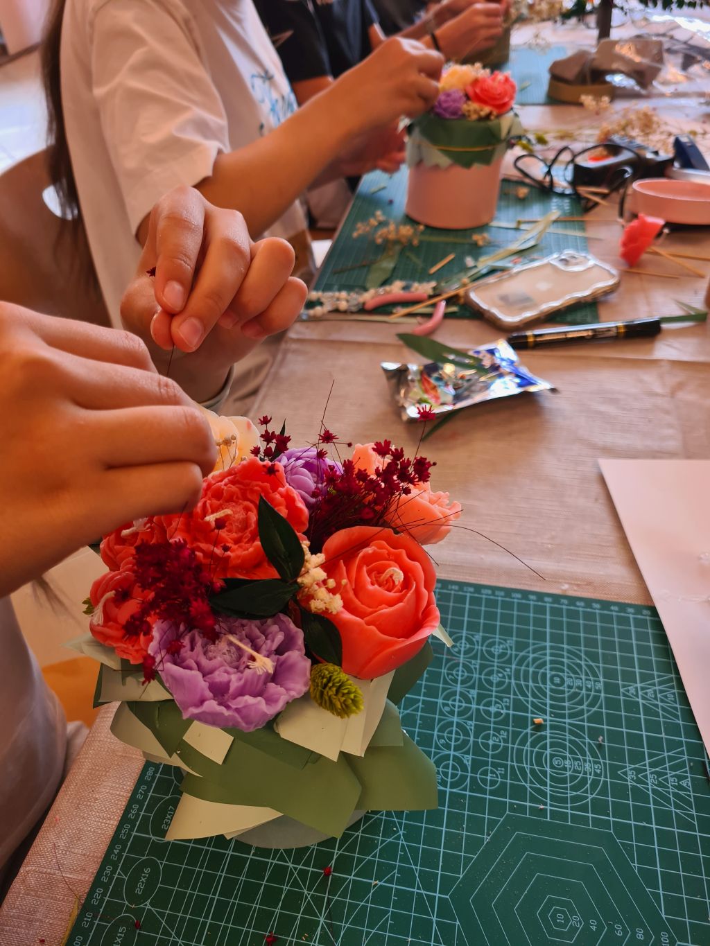 Uczestniczka umieszcza drobne bordowe suszone kwiaty między koralowymi i fioletowymi świecami w flowerboxie.
