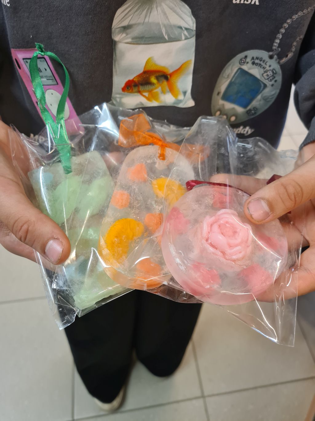 Uczestniczka prezentuje trzy własnoręcznie wykonane mydełka z efektem 3D. W przezroczystej bazie widoczne są kolorowe kwiaty i drobne dekoracje.