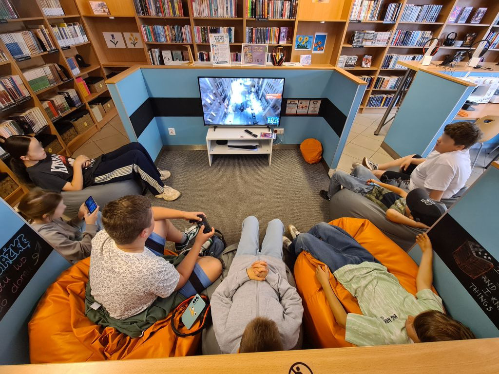 Młodzież odpoczywa na pufach i gra na PlayStation 5.