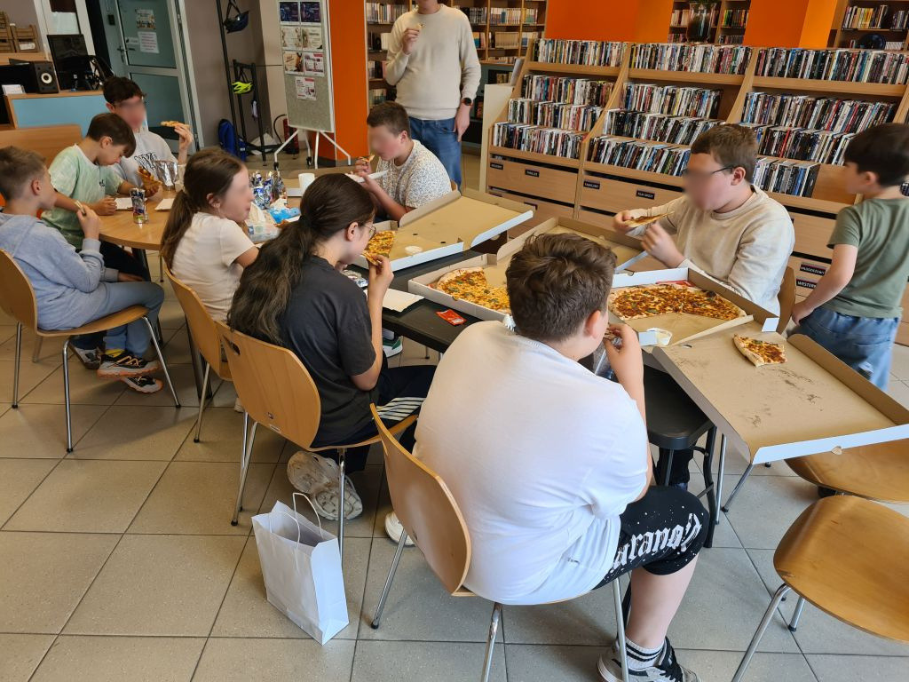 Uczestnicy warsztatów jedzą wspólnie pizzę przy stołach.