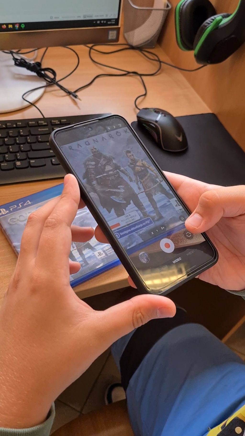Dłonie trzymające smartfon, na którego ekranie włączona jest aplikacja aparatu z widoczną grafiką z gry