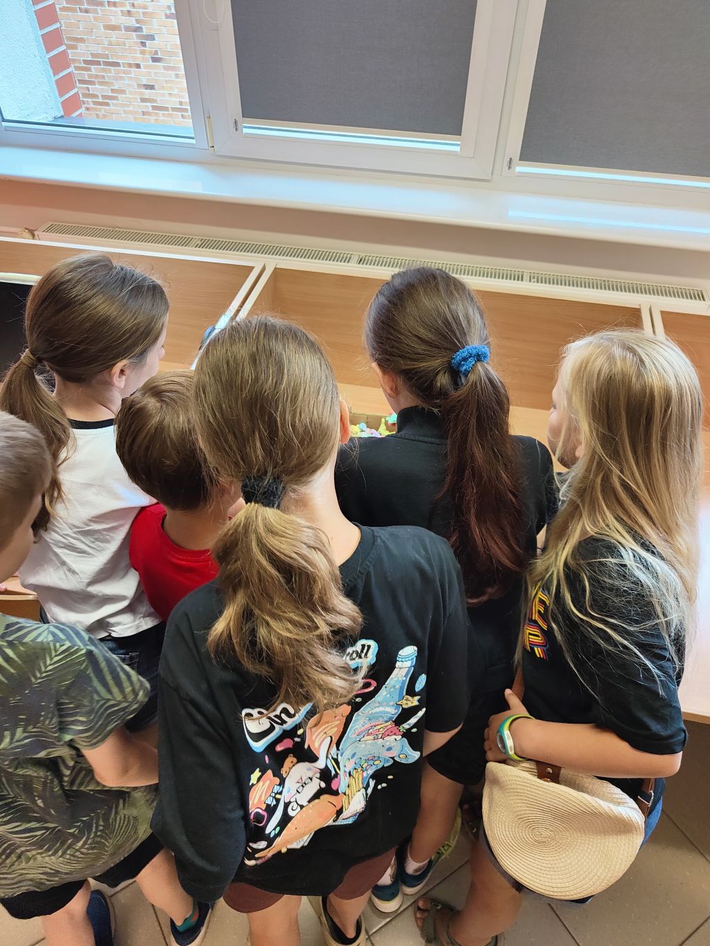 Grupa dzieci z bliska, widoczna od tyłu, zagląda razem do wnętrza otwartego pudełka.