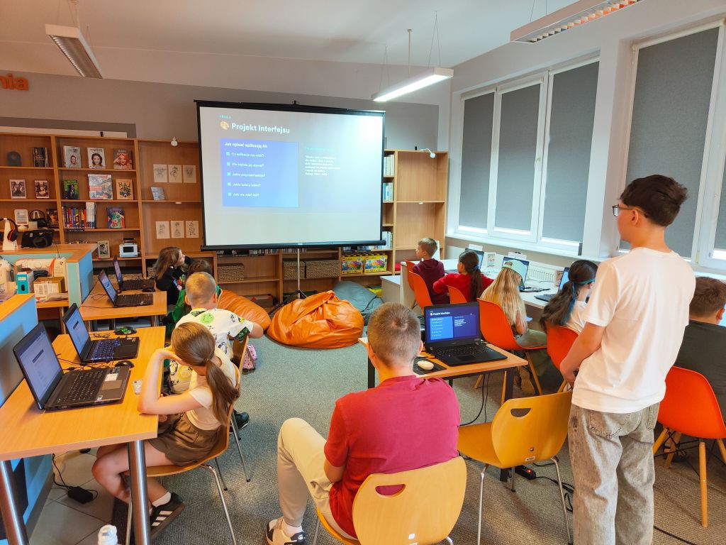 Uczniowie i instruktor w sali komputerowej oglądają prezentację 