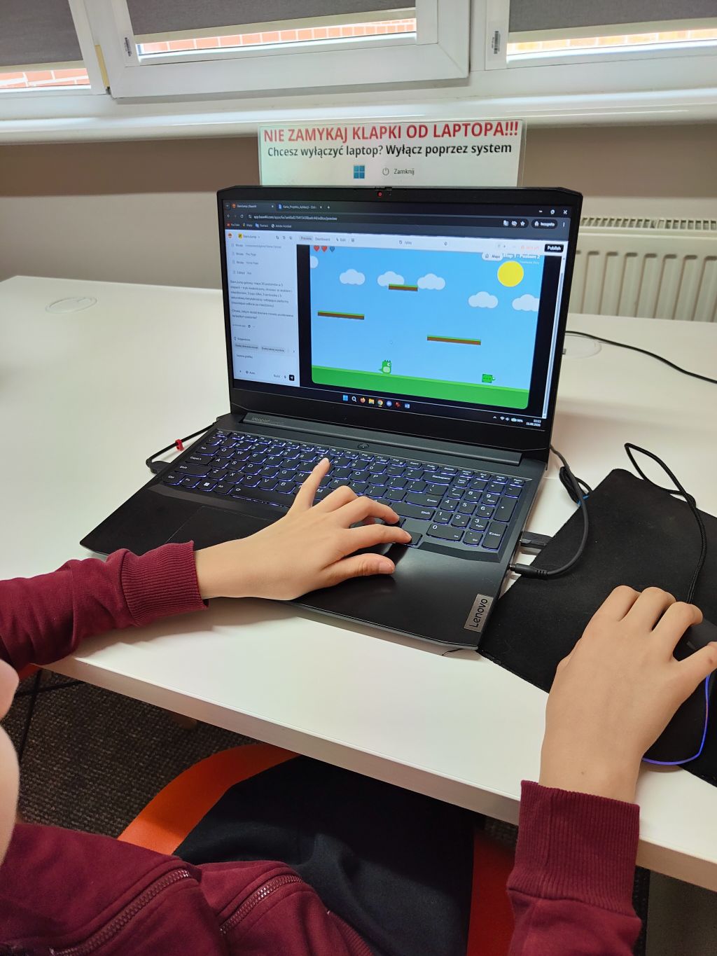 Zbliżenie na ręce dziecka grającego w grę platformową na laptopie Lenovo z podświetlaną klawiaturą.