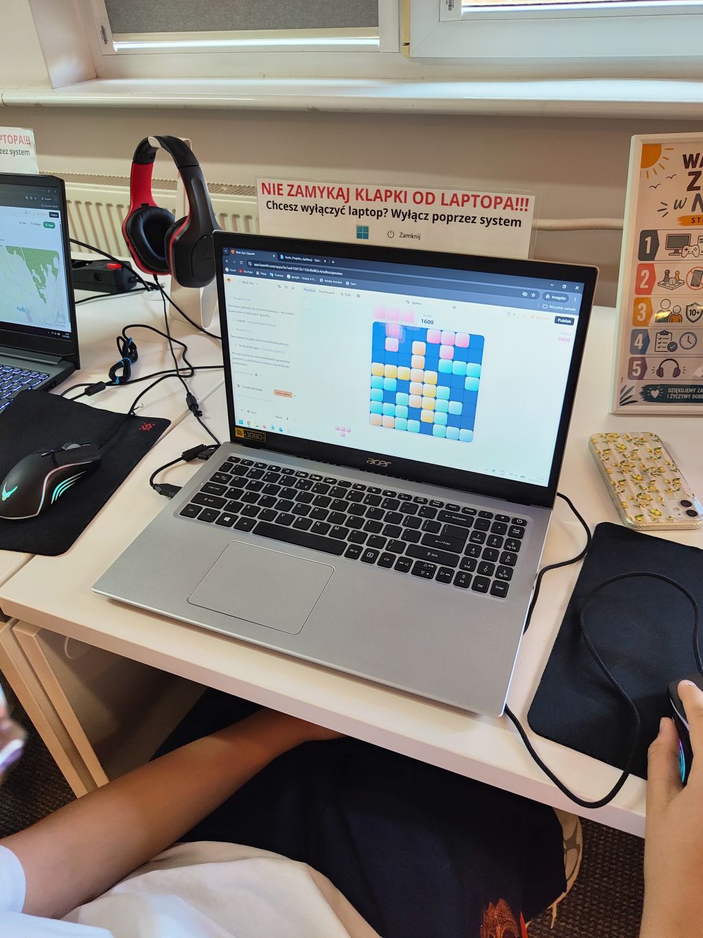 Srebrny laptop Acer na biurku, na którego ekranie widać otwartą grę logiczną z kolorowymi klockami.