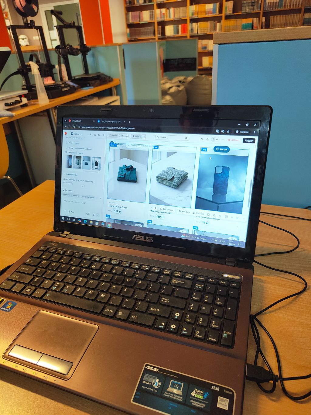 Otwarty laptop Asus na drewnianym stole, na ekranie widoczna jest strona sklepu internetowego z ubraniami i akcesoriami.