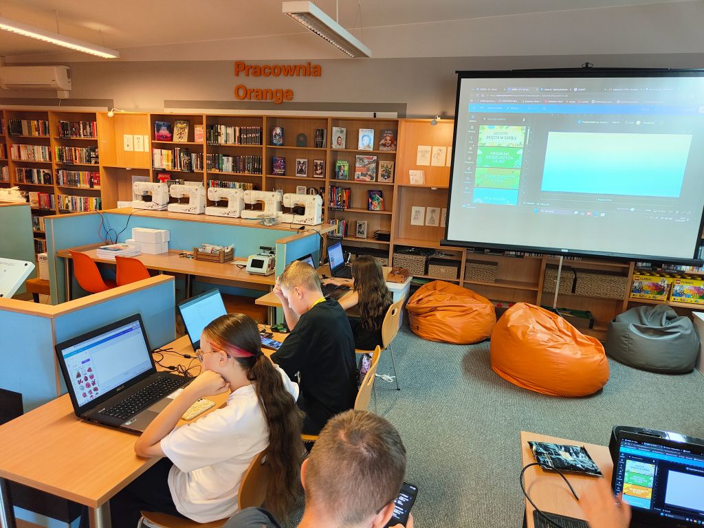 Widok z góry na przestrzeń Pracowni Orange z półkami pełnymi książek, maszynami do szycia, pufami i stanowiskami komputerowymi.