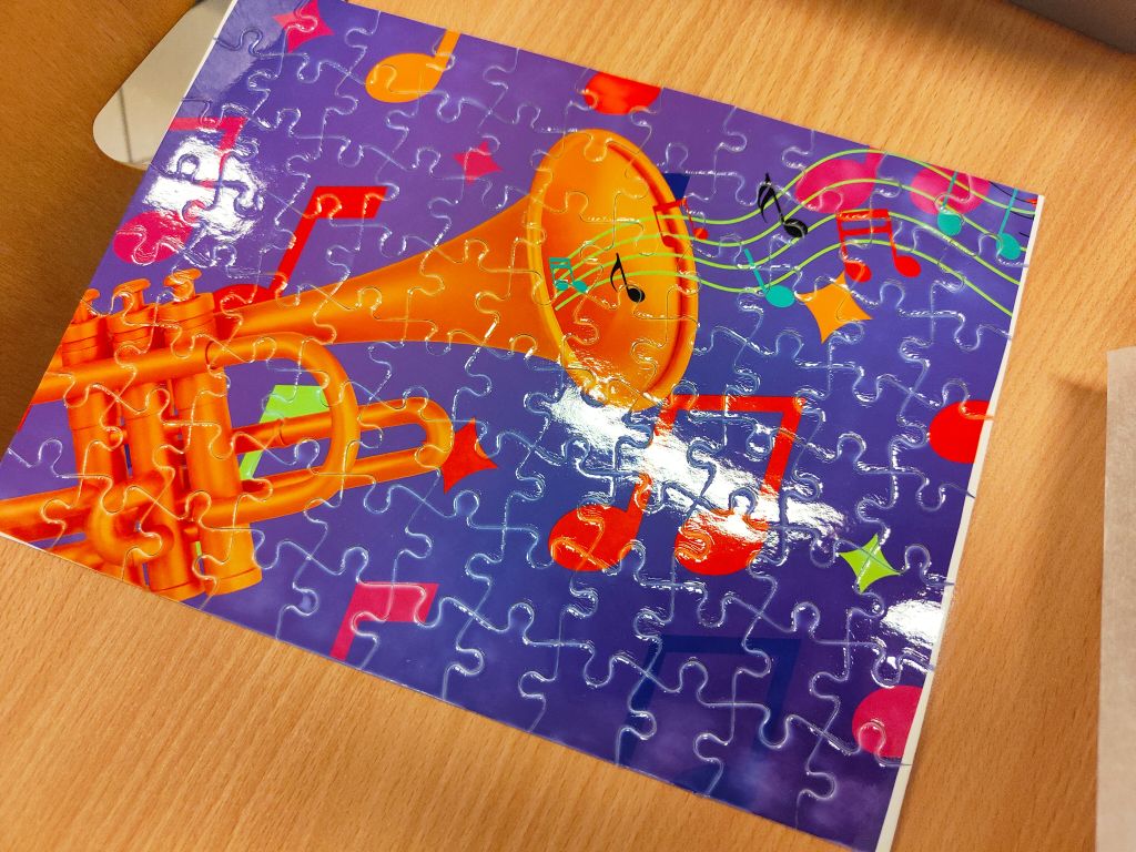 Gotowe puzzle z grafiką trąbki, nut i motywów muzycznych na fioletowym tle.