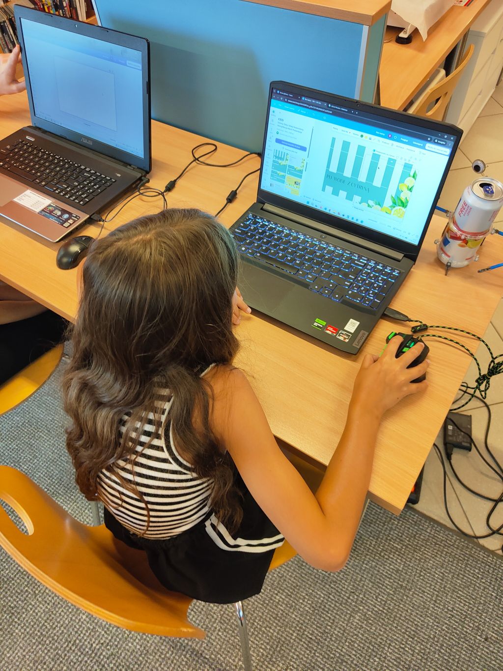 Widok z góry na dziewczynkę siedzącą przy biurku i korzystającą z myszki oraz laptopa do projektowania grafiki.