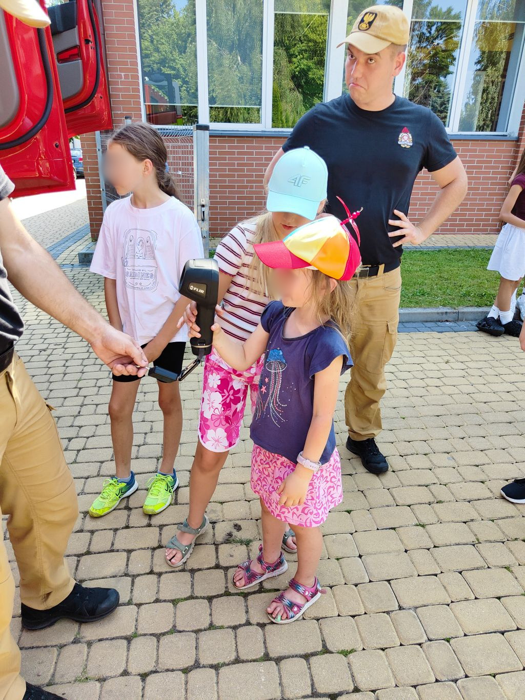 Dziewczynka z pomocą strażaka trzyma i testuje kamerę termowizyjną.