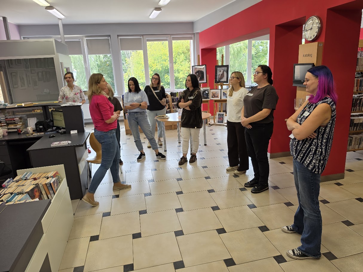 Grupa uczestniczek spotkania sieciującego stoi w pomieszczeniu biblioteki podczas rozmowy i zwiedzania.