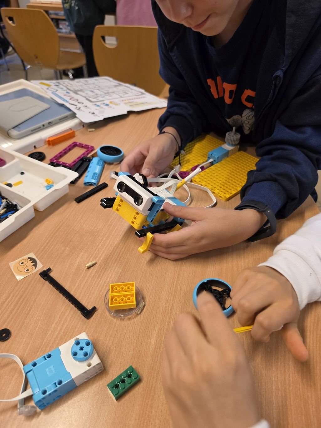 Uczestnik warsztatów składa robota z elementów LEGO Education przy stole. Wokół leżą części konstrukcyjne, instrukcje i tablet.