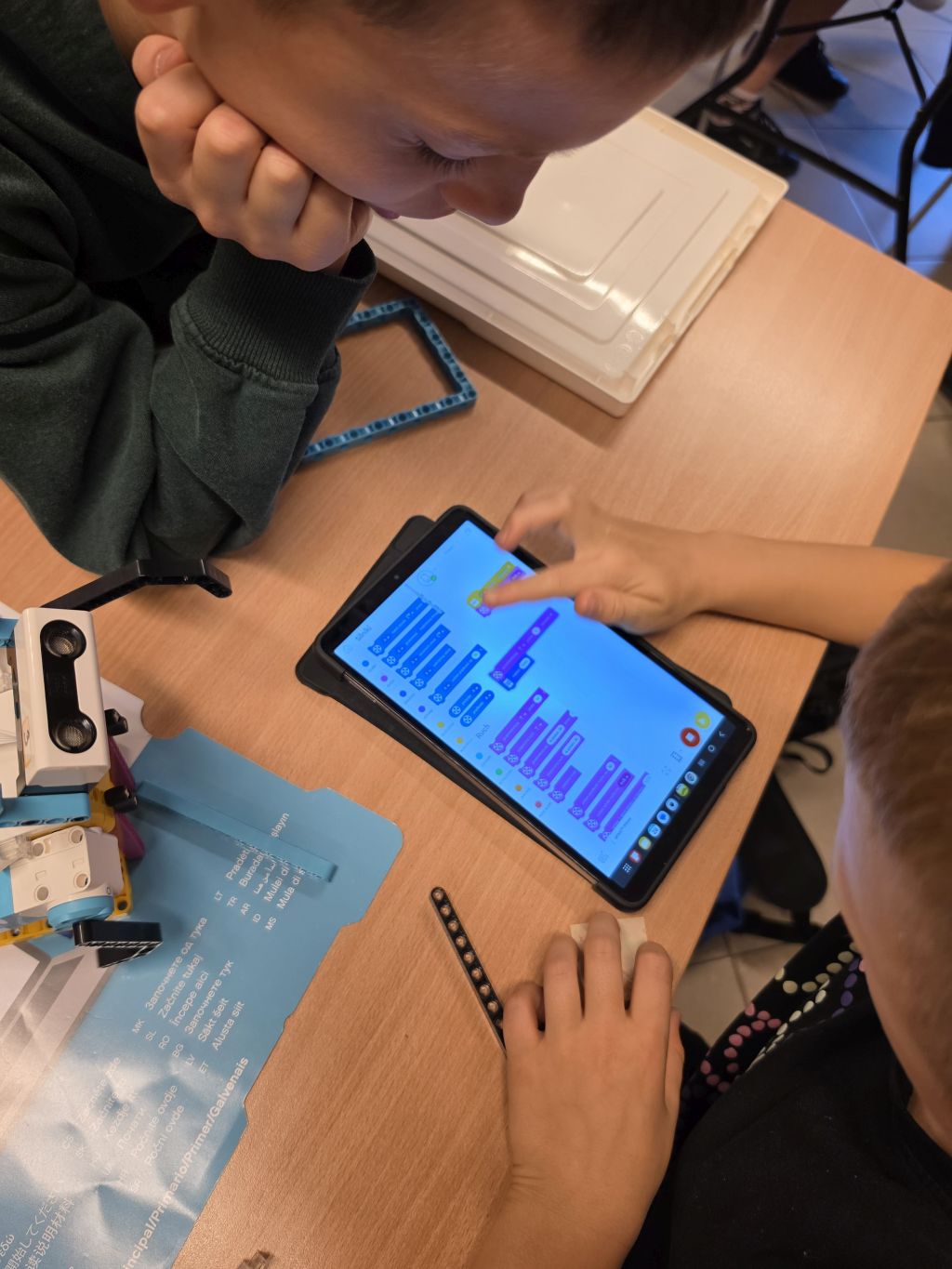 Dwoje uczestników programuje robota LEGO na tablecie. Obok na stole znajduje się zbudowana konstrukcja z czujnikiem.