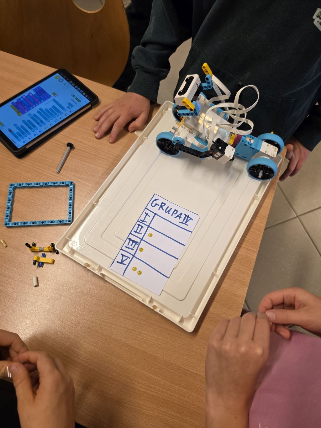 Uczestnicy testują zbudowanego robota LEGO na białej podstawie. Obok leży tablet z otwartym programem oraz karta z punktacją grupy.