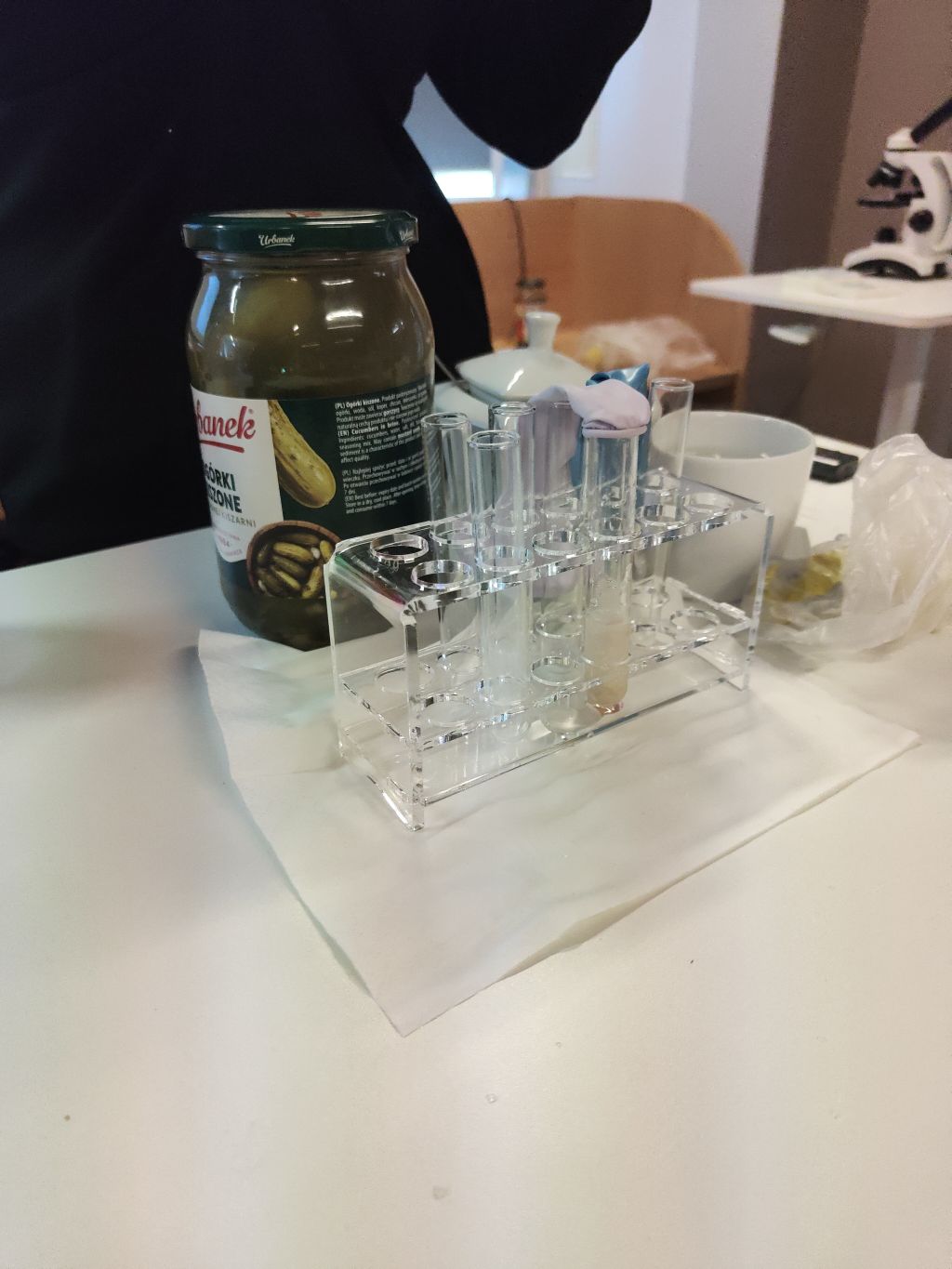 Stojak z probówkami laboratoryjnymi stojący obok słoika z ogórkami kiszonymi.