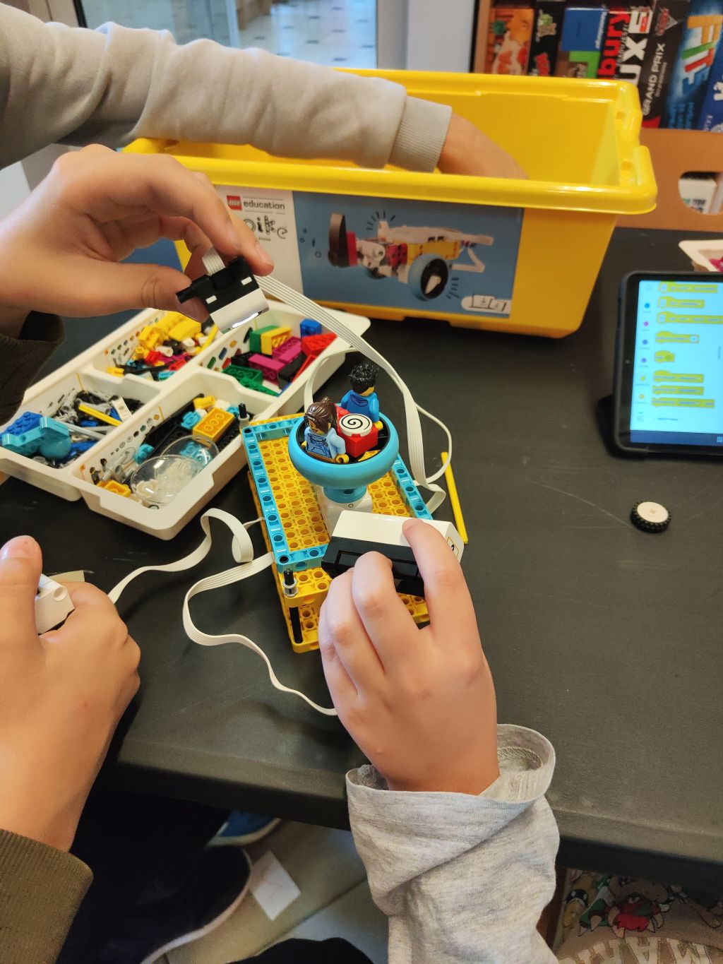 Uczestnicy montują czujniki i elementy na robocie LEGO. Obok znajduje się tablet z otwartym programem do kodowania.