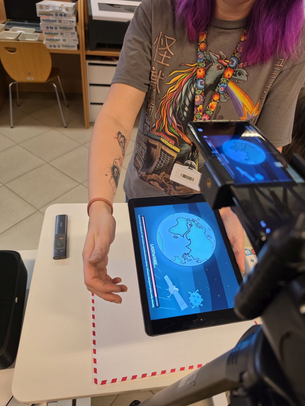 Zbliżenie na tablet wyświetlający aplikację edukacyjną trzymany przez prowadzącą.
