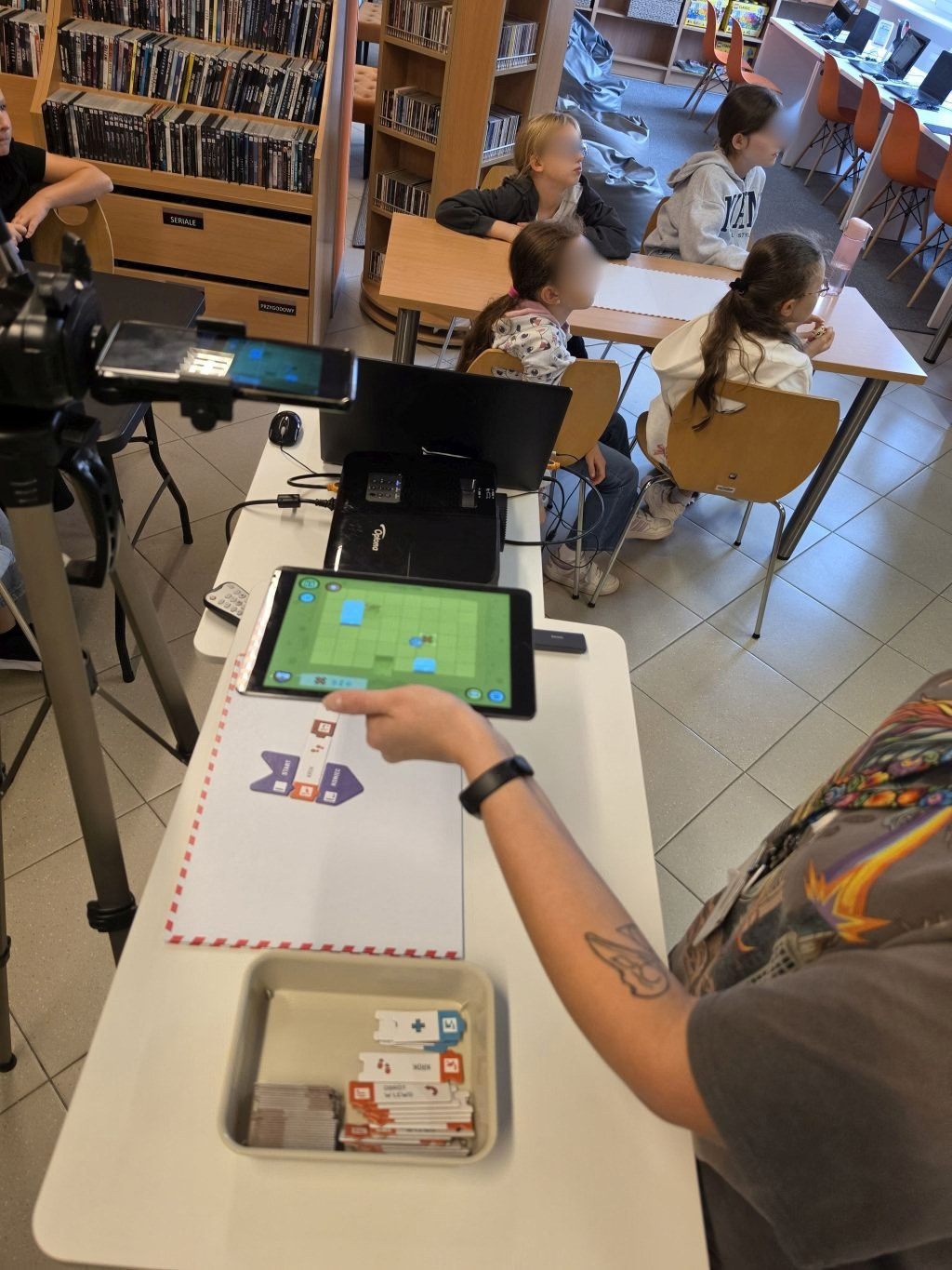 Prezentacja aplikacji na tablecie przy stoliku z matą i organizerem z klockami.