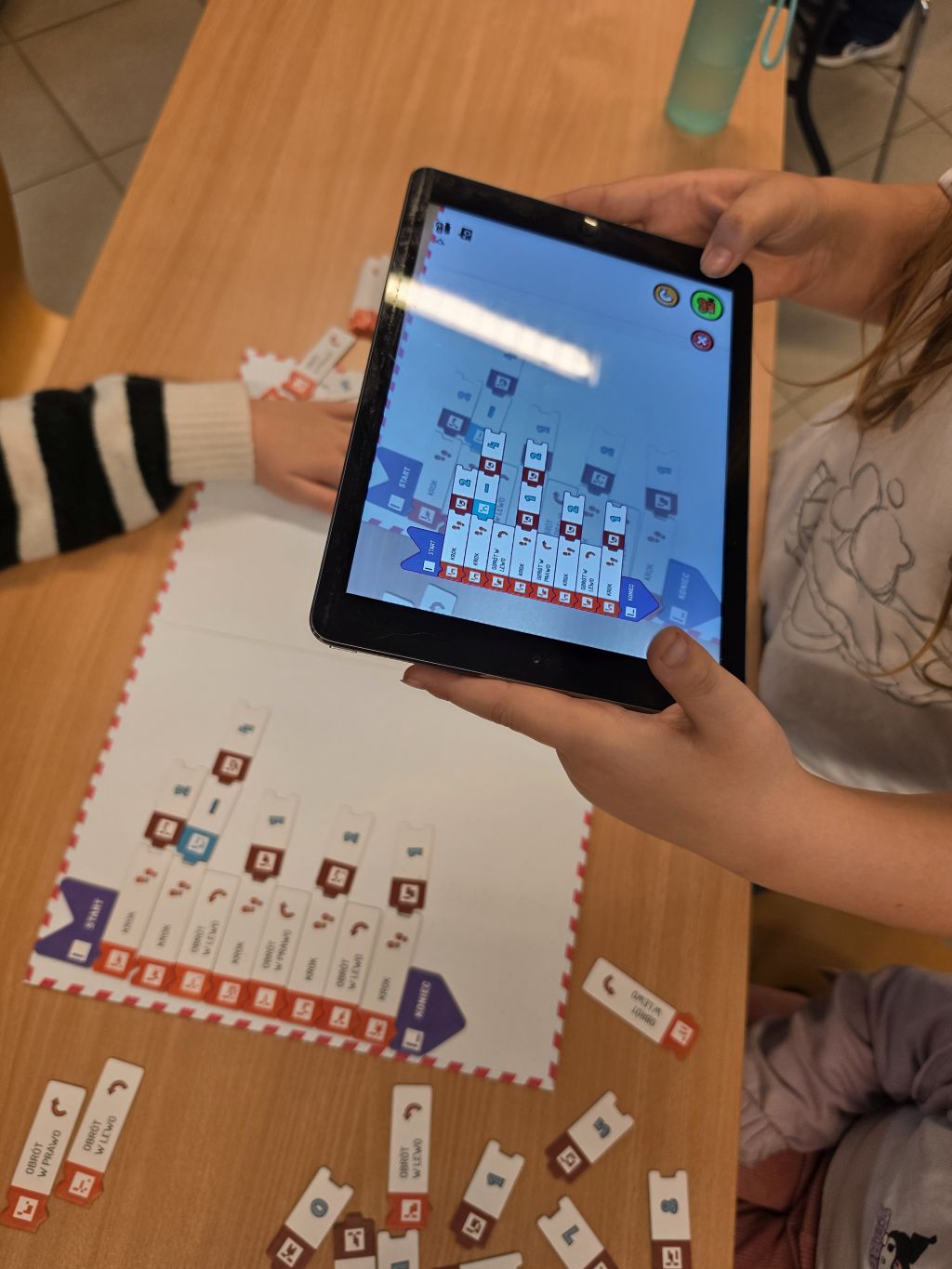 Dziecko pokazujące ekran tablet z widocznym programem blokowym nad matą.